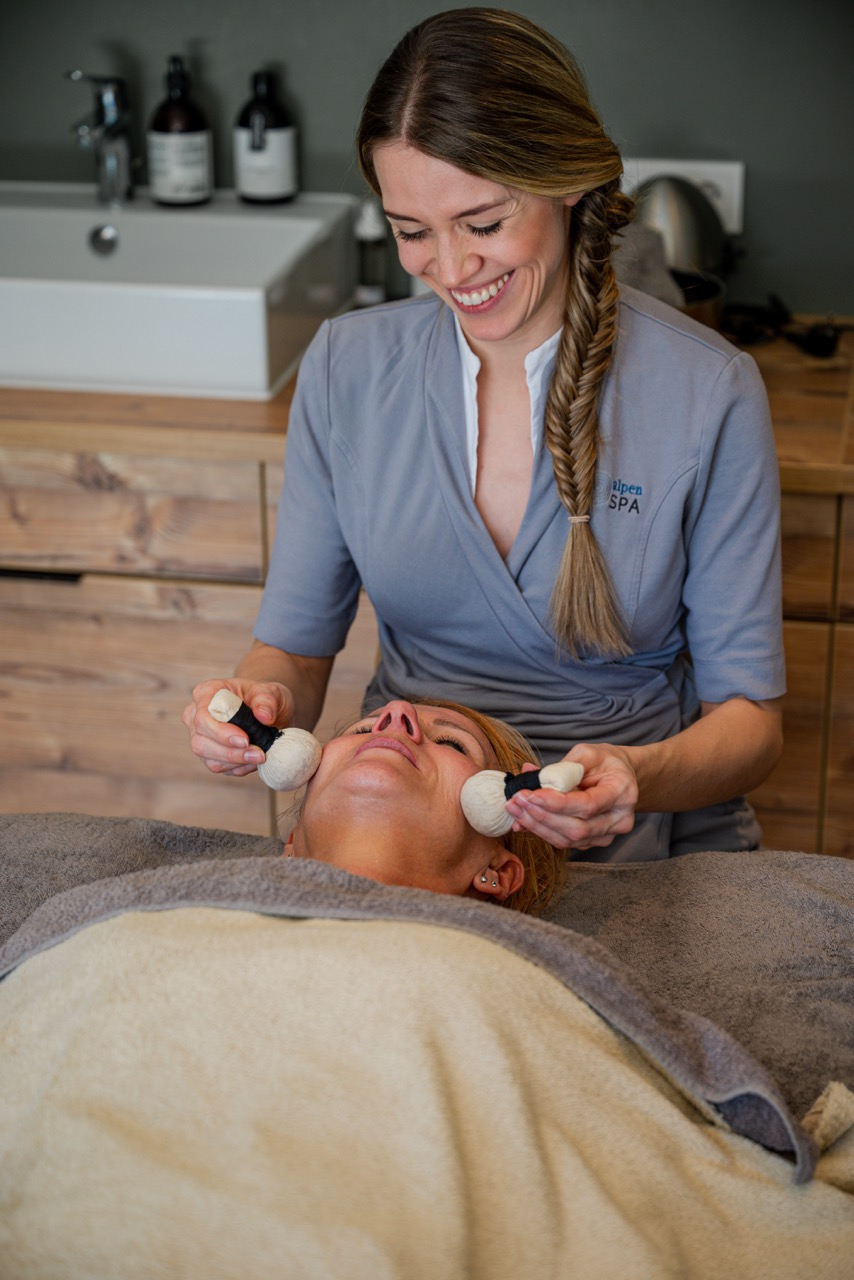 Spa-Therapeutin bei einer Gesichtsbehandlung mit Kräuterstempeln