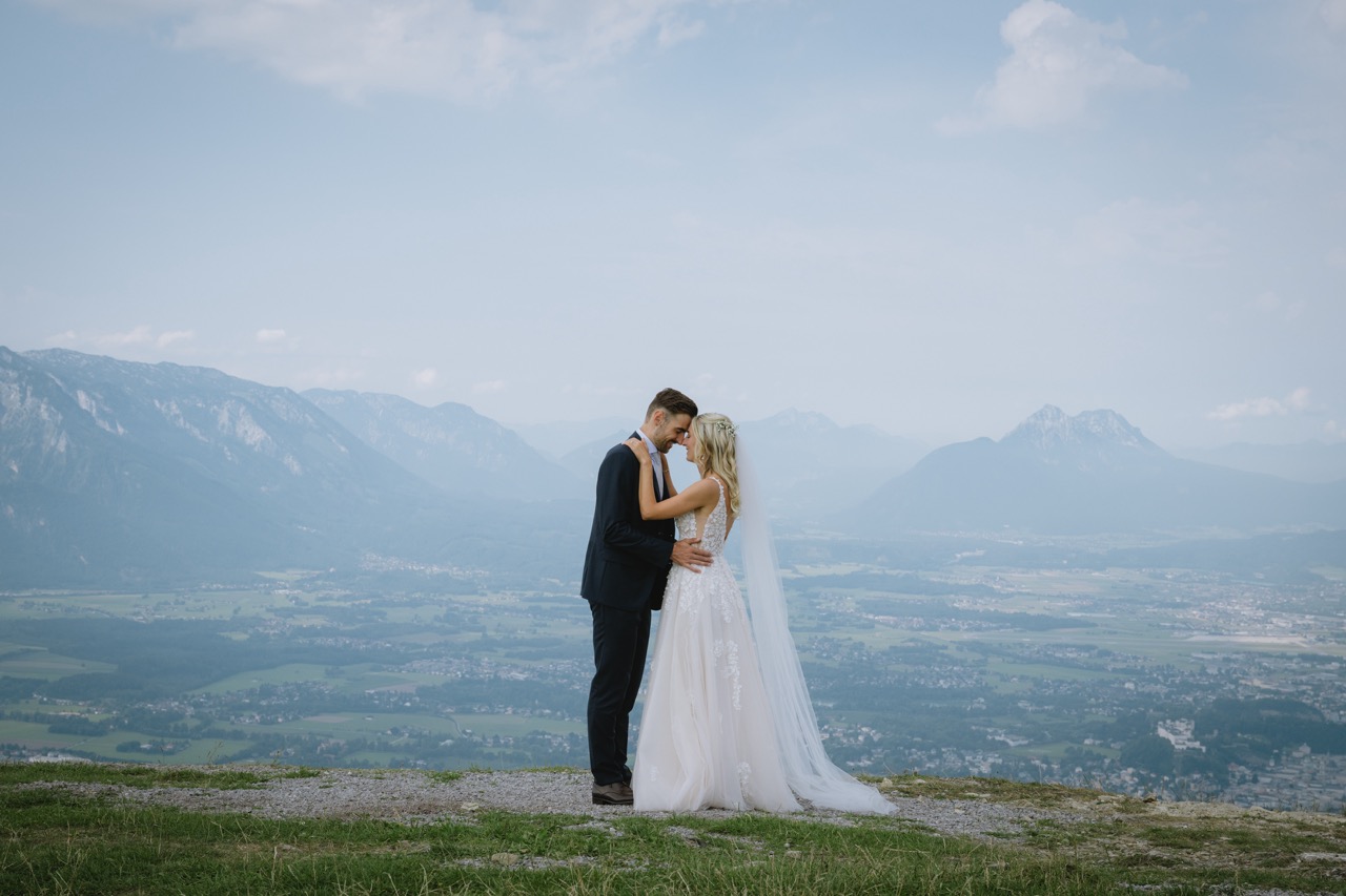 Brautpaar umarmt sich auf einem Berggipfel mit Alpenpanorama im Hintergrund