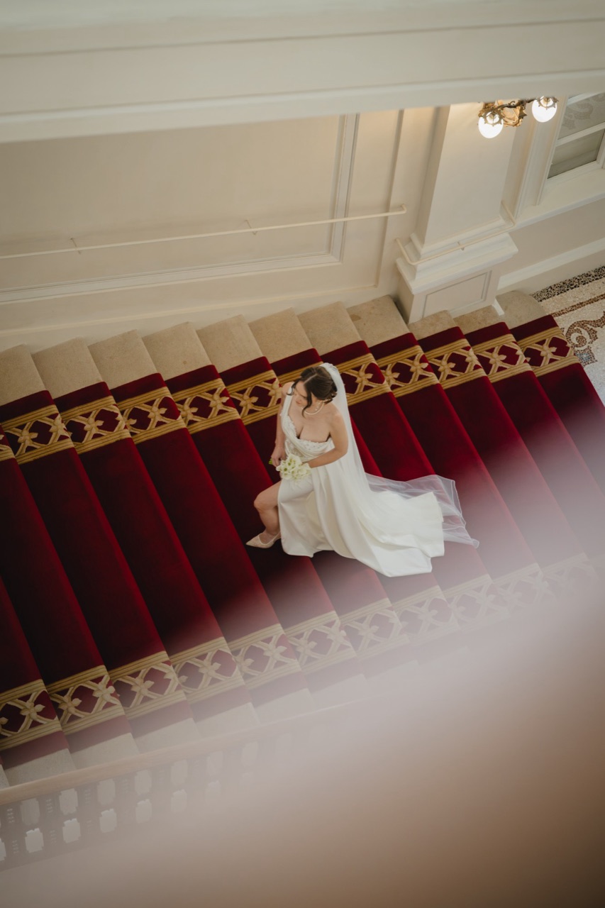 Braut mit Calla-Strauss auf rotem Treppenläufer — Aufnahme von oben in einem Wiener Palais