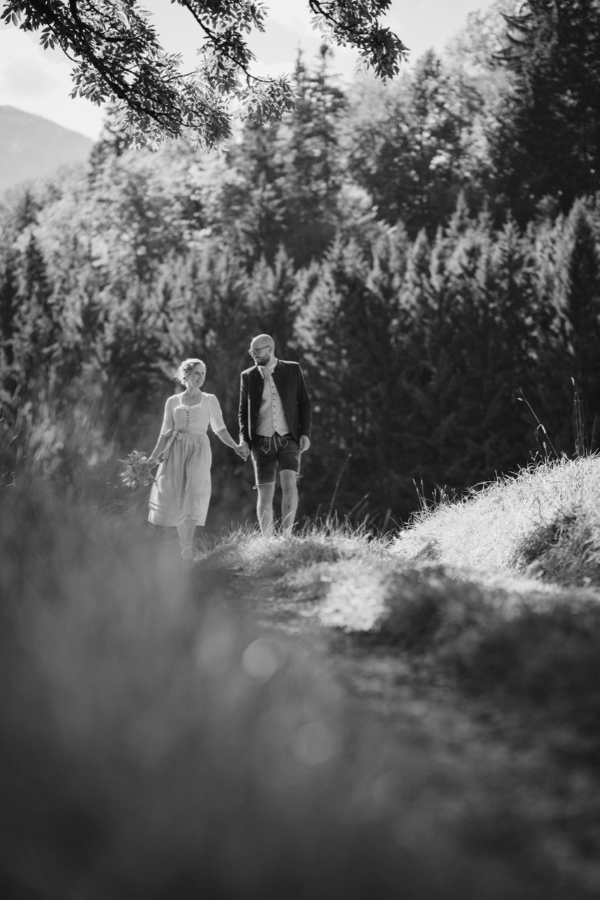 Brautpaar in Tracht geht Hand in Hand einen sonnigen Waldweg entlang — Schwarzweiss